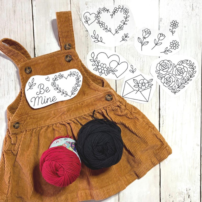 May include: A brown corduroy pinafore dress with a "Be Mine" patch and floral heart designs. Includes red and black yarn skeins, and several heart and floral embroidery patterns. The dress has button details.