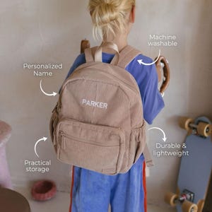 May include: A tan corduroy backpack with the name "PARKER" embroidered in white. The backpack has a front pocket and adjustable straps. Features include practical storage, machine washability, and a durable, lightweight design.
