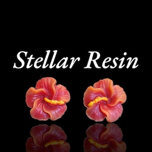 May include: Two resin hibiscus flower earrings in shades of red and orange with yellow centers. The earrings are displayed on a black background with a reflection. The text "Stellar Resin" is above the earrings.