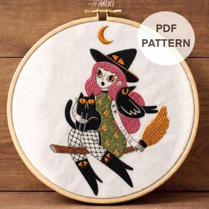 May include: Embroidered hoop art featuring a witch with pink hair, a black cat, and a crow, all riding a broom. The witch wears a black hat and green dress. The text "PDF PATTERN" and "DMC Color Chart + Stitch Guide" are visible.