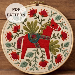 May include: An embroidery hoop containing a fabric piece with a red horse design, floral motifs, and green leaves. The text "PDF PATTERN" appears in the upper left, and "DMC Color Chart + Stitch Guide" is printed at the bottom of the image.