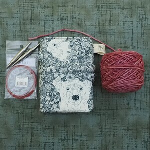 May include: A rectangular fabric case featuring a black and white floral and bear print, a circular red knitting needle cable in a clear plastic package with two metal needle tips, and a ball of dark pink yarn with a loose strand of yarn.