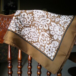 May include: A brown paisley patterned bandana with white accents. The bandana is draped over a wooden chair.