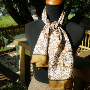 May include: A brown and white patterned scarf with a gold trim. The scarf is tied around a mannequin's neck.