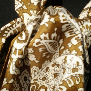 May include: A brown and white patterned silk scarf with a paisley design. The scarf is tied in a knot.