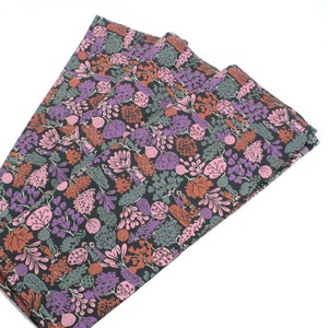 May include: A stack of three fabric napkins with a floral pattern in shades of pink, purple, green, and brown on a black background.