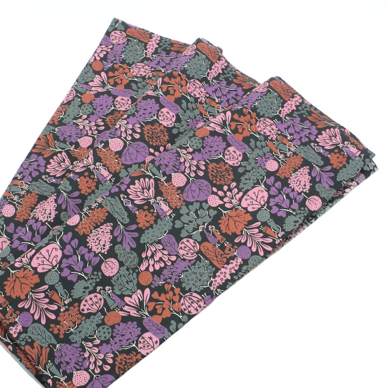 May include: A stack of three fabric napkins with a floral pattern in shades of pink, purple, green, and brown on a black background.