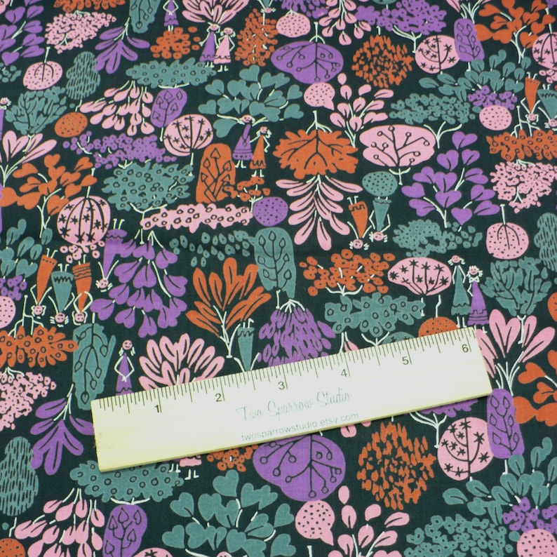 May include: A dark green fabric with a repeating pattern of pink, purple, orange, and white stylized trees and figures. A ruler with the text "Two Sparrow Studio" is placed on top of the fabric.