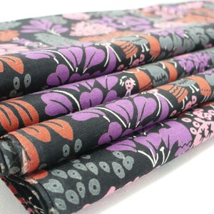 May include: Close-up of a black fabric with a colorful floral pattern. The fabric is folded in layers, revealing the intricate details of the design. The pattern features pink, purple, and orange flowers with white outlines.