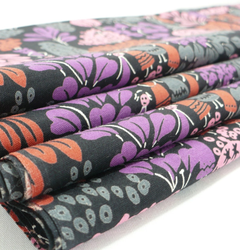 May include: Close-up of a black fabric with a colorful floral pattern. The fabric is folded in layers, revealing the intricate details of the design. The pattern features pink, purple, and orange flowers with white outlines.