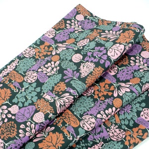 May include: Black fabric with a repeating pattern of stylized flowers, leaves, and figures in shades of pink, purple, brown, and green.