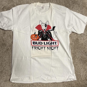 May include: White t-shirt featuring a Halloween-themed graphic. The design includes a cartoon dog dressed as a vampire, a jack-o'-lantern, a bat, and a ghost. The text "BUD LIGHT FRIGHT NIGHT" is displayed in a red and blue banner.