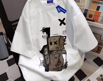 May include: White short-sleeved t-shirt featuring a graphic of a person with a paper bag over their head, holding a coffee cup. The graphic is in shades of brown and black, with an 'X' symbol. A blue tag is attached to the shirt.