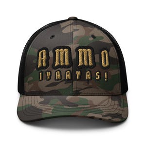 May include: Camouflage trucker hat with the word "AMMO" embroidered in gold lettering above "IYRRAYRS!". The hat features a black mesh back and a curved brim, perfect for outdoor activities or casual wear.