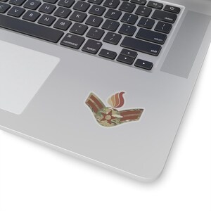 May include: A sticker featuring a camouflage pattern with a red star and a flame design. The sticker is on a silver laptop.