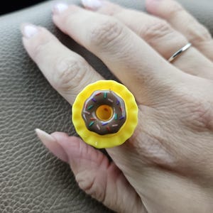 Könnte beinhalten: Ein gelber Ring mit einem braunen und weißen Donut-Design. Der Donut hat bunte Streusel.