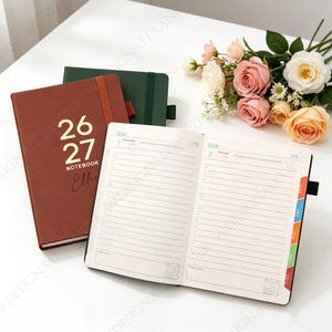 May include: A selection of notebooks, one open to reveal lined pages. The nearest notebook has a brown cover with gold text reading "26 27 NOTEBOOK Ellie". A green notebook and a bouquet of roses are also in view.