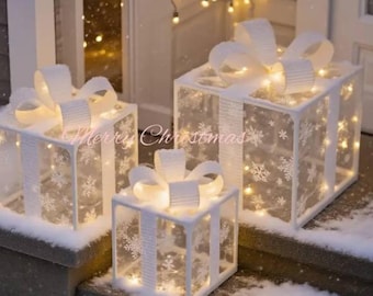 May include: Three illuminated Christmas gift boxes with white bows and snowflake patterns. The boxes are lit from within, creating a warm glow. The text "Merry Christmas" is visible on the front of the boxes. The boxes are sitting on a snowy surface.