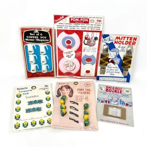 Könnte beinhalten: Eine Sammlung von Vintage-Bastelzubehör, darunter Pomponmacher, Spangen, Fäustlingshalter und Memo-Magnete. Die Artikel sind in farbenfrohem Karton mit Text und Illustrationen verpackt und zeigen eine Retro-Ästhetik.