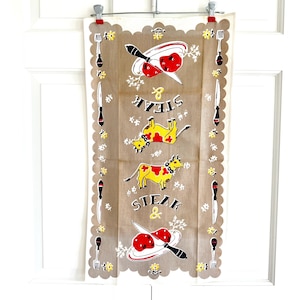 May include: Vintage kitchen towel with a brown background, featuring illustrations of steak and cows. The towel has a scalloped edge with alternating knife and fork designs. The words "STEAK & STEAK" are printed on the towel.