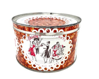 May include: A round metal tin featuring a red and white graphic print of people at a party. The text reads Katy's Nuts and Always the hit of the party. The background pattern shows brown nuts, and the lid has a scalloped white border design.