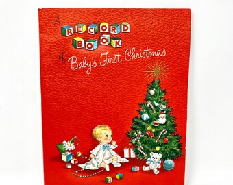 May include: A red record book titled "A Record Book of Baby's First Christmas." The cover features a baby in a white robe, a decorated Christmas tree, and colourful blocks. The book has a textured surface.