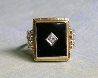May include: A gold-toned ring with a square black onyx center stone. A small diamond is set in the center of the onyx. The ring has decorative side accents and a rectangular shape.