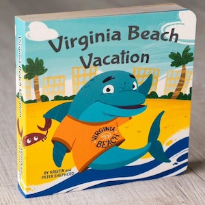 Puede incluir: Una portada de libro infantil con un delf&iacute;n de dibujos animados que lleva una camisa naranja con las palabras "Virginia Beach" en ella. El delf&iacute;n est&aacute; en una playa con palmeras y edificios en el fondo. El t&iacute;tulo del libro es "Virginia Beach Vacation" y el autor es Kristin y Peter Shepherd.