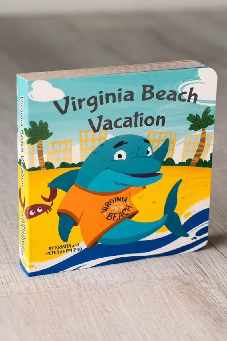 Puede incluir: Una portada de libro infantil con un delf&iacute;n de dibujos animados que lleva una camisa naranja con las palabras "Virginia Beach" en ella. El delf&iacute;n est&aacute; en una playa con palmeras y edificios en el fondo. El t&iacute;tulo del libro es "Virginia Beach Vacation" y el autor es Kristin y Peter Shepherd.