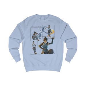 May include: A light blue sweatshirt with a graphic of Korra from The Legend of Korra. The graphic shows Korra in four different poses, each representing a different element: water, earth, fire, and air. The text 'The Legend of Korra' is printed above the graphic.