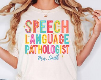 May include: Ivory-colored t-shirt with the words "SPEECH LANGUAGE PATHOLOGIST" in colorful, bold letters. The name "Mrs. Smith" is written in a light blue script font below the main text. The word "IVORY" is written in a black script font in the bottom right corner.