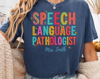 May include: A navy blue t-shirt with the words "SPEECH LANGUAGE PATHOLOGIST" in colorful, bold letters. The name "Mrs. Smith" is printed below the text. The shirt is labeled "Denim" at the bottom.
