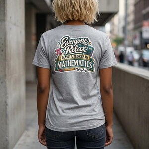 May include: A heather gray short-sleeve t-shirt featuring a graphic on the back with the text "Everyone Relax I HAVE A DEGREE IN MATHEMATICS". The design includes a pi symbol, a calculator, a pencil, and the mathematical formula a²+b²=c².