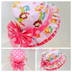 May include: Pink sun hat with a white polka dot bow and a pink ruffle trim. The hat is decorated with a mermaid print featuring colorful mermaids and seashells.