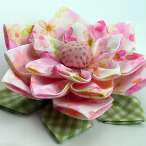 K&ouml;nnte beinhalten: Eine rosa und wei&szlig;e Stoffblume mit gr&uuml;nem kariertem Untergrund. Die Blume hat eine Mitte aus rosa und grauem Stoff mit wei&szlig;en Punkten.