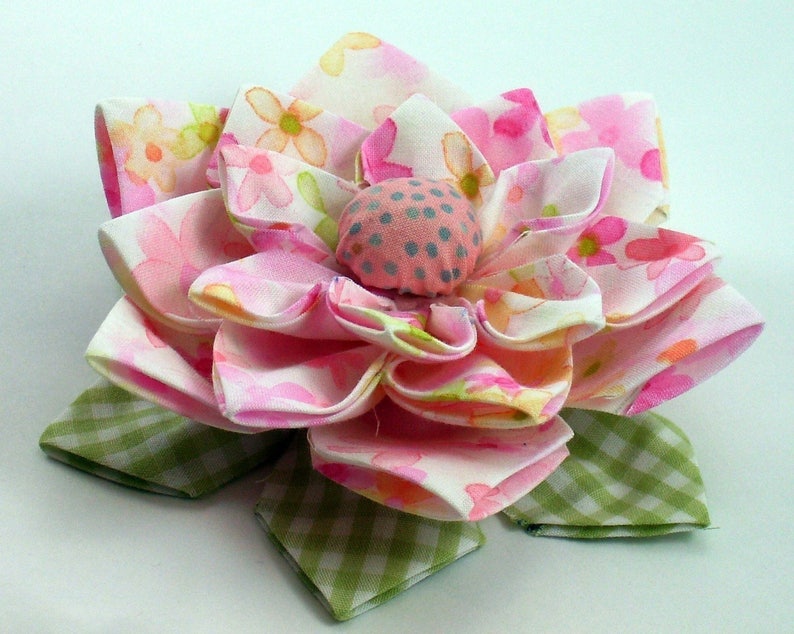 K&ouml;nnte beinhalten: Eine rosa und wei&szlig;e Stoffblume mit gr&uuml;nem kariertem Untergrund. Die Blume hat eine Mitte aus rosa und grauem Stoff mit wei&szlig;en Punkten.