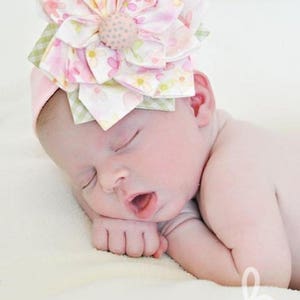 K&ouml;nnte beinhalten: Ein schlafendes Baby tr&auml;gt ein rosa Stirnband mit einer gro&szlig;en, mehrfarbigen Bl&uuml;te aus Stoff. Das Stirnband ist aus weichem, dehnbarem Stoff und perfekt f&uuml;r Neugeborene und Kleinkinder.