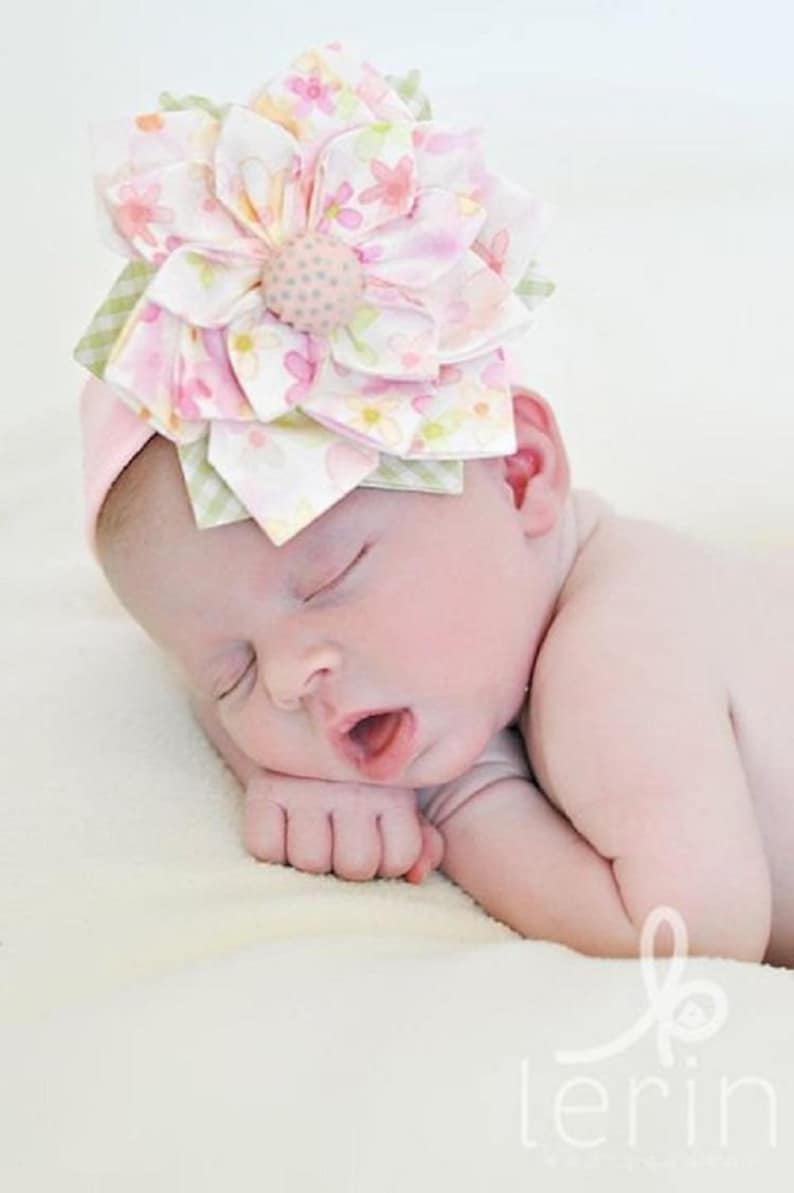 K&ouml;nnte beinhalten: Ein schlafendes Baby tr&auml;gt ein rosa Stirnband mit einer gro&szlig;en, mehrfarbigen Bl&uuml;te aus Stoff. Das Stirnband ist aus weichem, dehnbarem Stoff und perfekt f&uuml;r Neugeborene und Kleinkinder.
