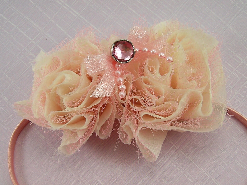 K&ouml;nnte beinhalten: Ein rosa-cremefarbenes Stoffhaarband mit einem rosa Strassstein-Verzierungen und Perlenakzenten.