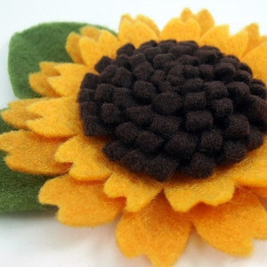 May include: A felt sunflower with a brown center and green leaves. The sunflower is yellow and has a textured, fuzzy appearance.