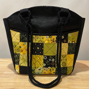 Peut inclure: Sac cabas noir avec un motif patchwork en jaune, vert et noir. Le sac a deux anses en corde noire.