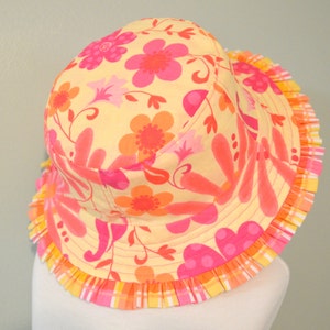 May include: A yellow sun hat with a pink and orange floral print and a pink and yellow ruffled trim.
