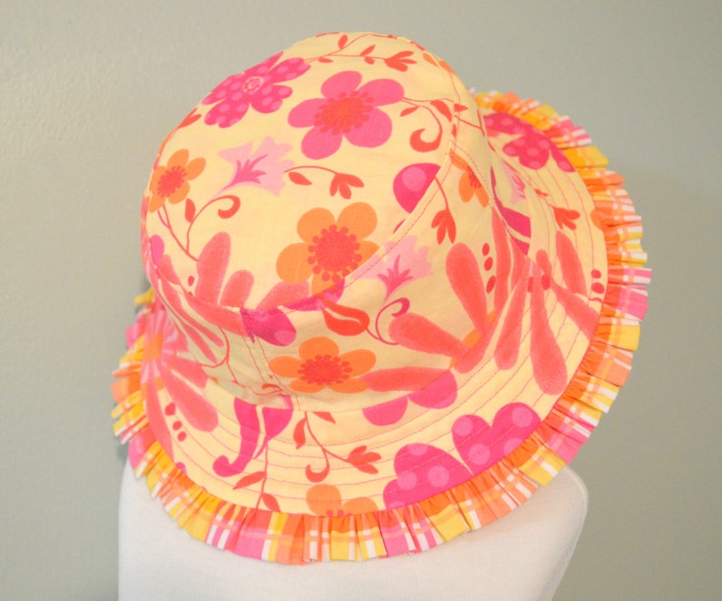 May include: A yellow sun hat with a pink and orange floral print and a pink and yellow ruffled trim.
