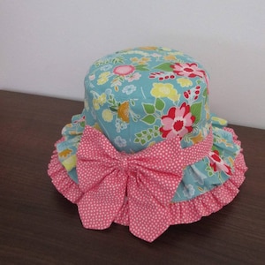 May include: A blue and pink sun hat with a floral print and a pink polka dot bow. The hat has a ruffled brim.