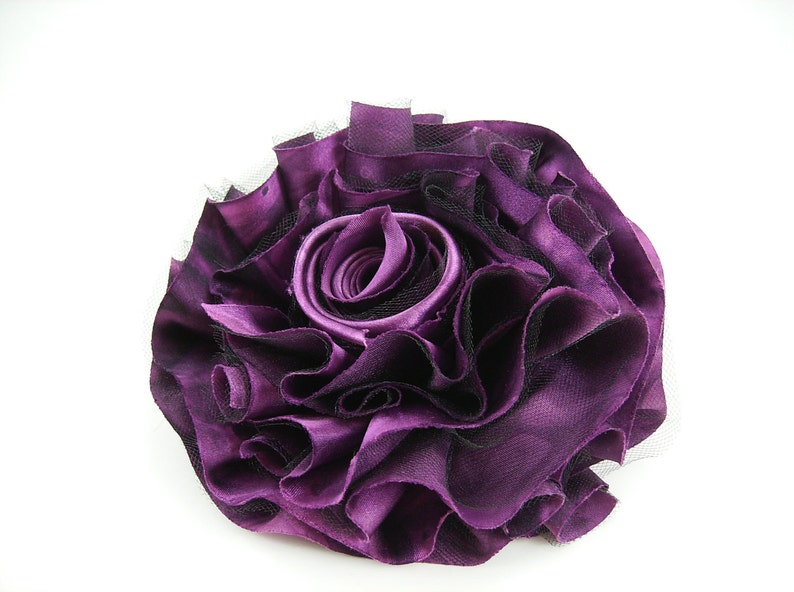 K&ouml;nnte beinhalten: Eine gro&szlig;e violette Stoffblume mit einer ger&uuml;schten Textur und schwarzen Netz-Akzenten.
