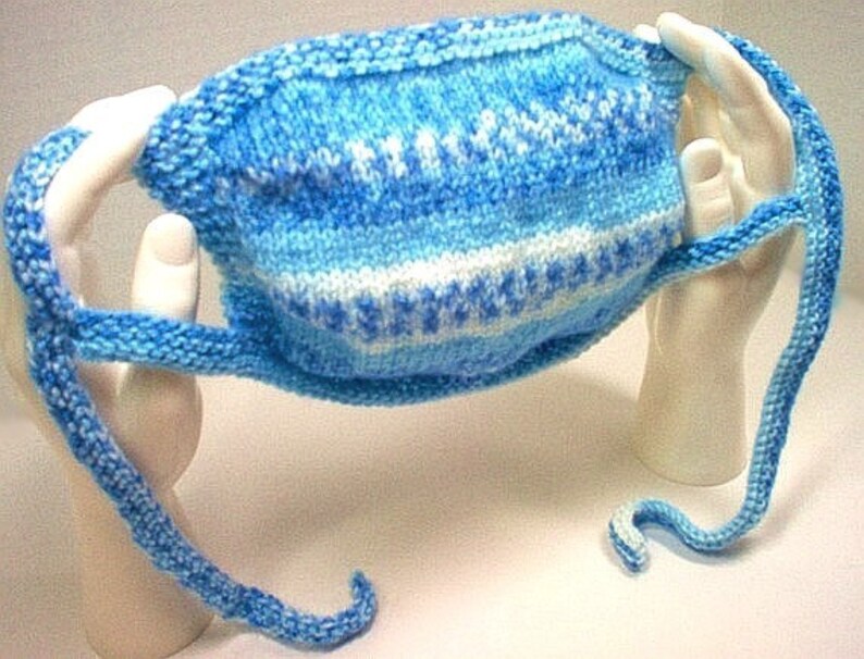 May include: A blue and white knitted face mask with long ties. The mask is made with a simple stitch pattern and has a white stripe in the middle.