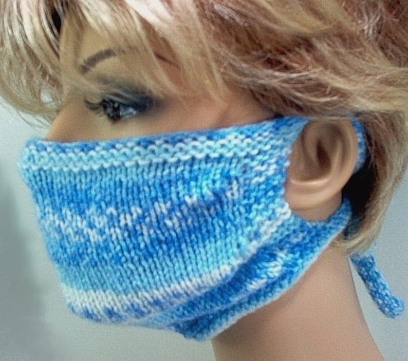 May include: A blue and white knitted face mask with a white tie. The mask is made with a simple knit stitch and has a white border.