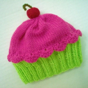 May include: A pink and green knitted hat shaped like a cupcake with a red cherry on top.