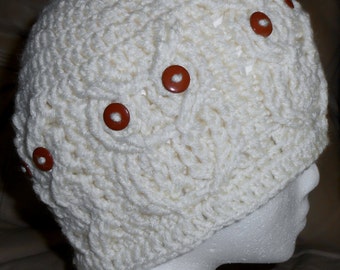 May include: White crocheted beanie with brown buttons. The beanie is on a white mannequin head.