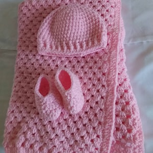May include: A handmade pink crochet baby set, including a blanket, hat, and booties. The blanket has a textured pattern, and the booties and hat are designed to match. The set is made of soft yarn.